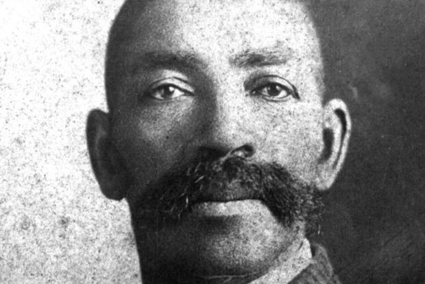 A historical black and white portrait of a man with a prominent mustache, dressed in formal attire.