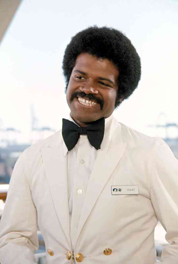 A smiling man wearing a white tuxedo with a black bow tie, standing in a bright indoor setting.